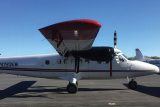 A small white propeller airplane with the registration N190KM is parked on an airstrip. It has a red-tipped nose and a visible wing. The sky is clear and blue in the background. Another aircraft is partially visible to the right.