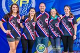 Five people are smiling and standing together in front of a blue banner with logos. They are wearing matching black, red, and blue sports jerseys with "Carolina SC Boogie Babes" written on them.