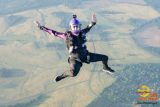 A person in a black jumpsuit and helmet skydives with arms spread wide. They wear a camera on their helmet and have a clear visor. Below, expansive green fields and winding roads are visible. The image has logos for Skydive Carolina and a date from 2019.