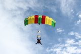 A person is parachuting in the sky with a green, yellow, and red parachute. The sky is partly cloudy, creating a picturesque background for the parachute descent.