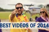 A man in sunglasses and a yellow shirt points at the camera while standing in front of a small airplane. A woman in a purple shirt and sunglasses stands beside him, both wearing colorful leis. Text overlay reads "BEST VIDEOS OF 2014.