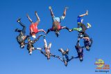 A group of nine skydivers form a circle while free-falling against a clear blue sky. Each diver is dressed in colorful gear, creating a vibrant display of human flight and teamwork.