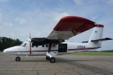 Twin-engine propeller aircraft with a red and white color scheme parked on an airport tarmac. The plane has a high wing design and the tail is marked with "N190KM". The door is open, displaying part of the interior. Sky is partly cloudy.