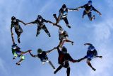 A group of eight skydivers in mid-air, forming a circle as they hold hands against a clear blue sky. They wear colorful jumpsuits and helmets, creating a dynamic and synchronized formation.