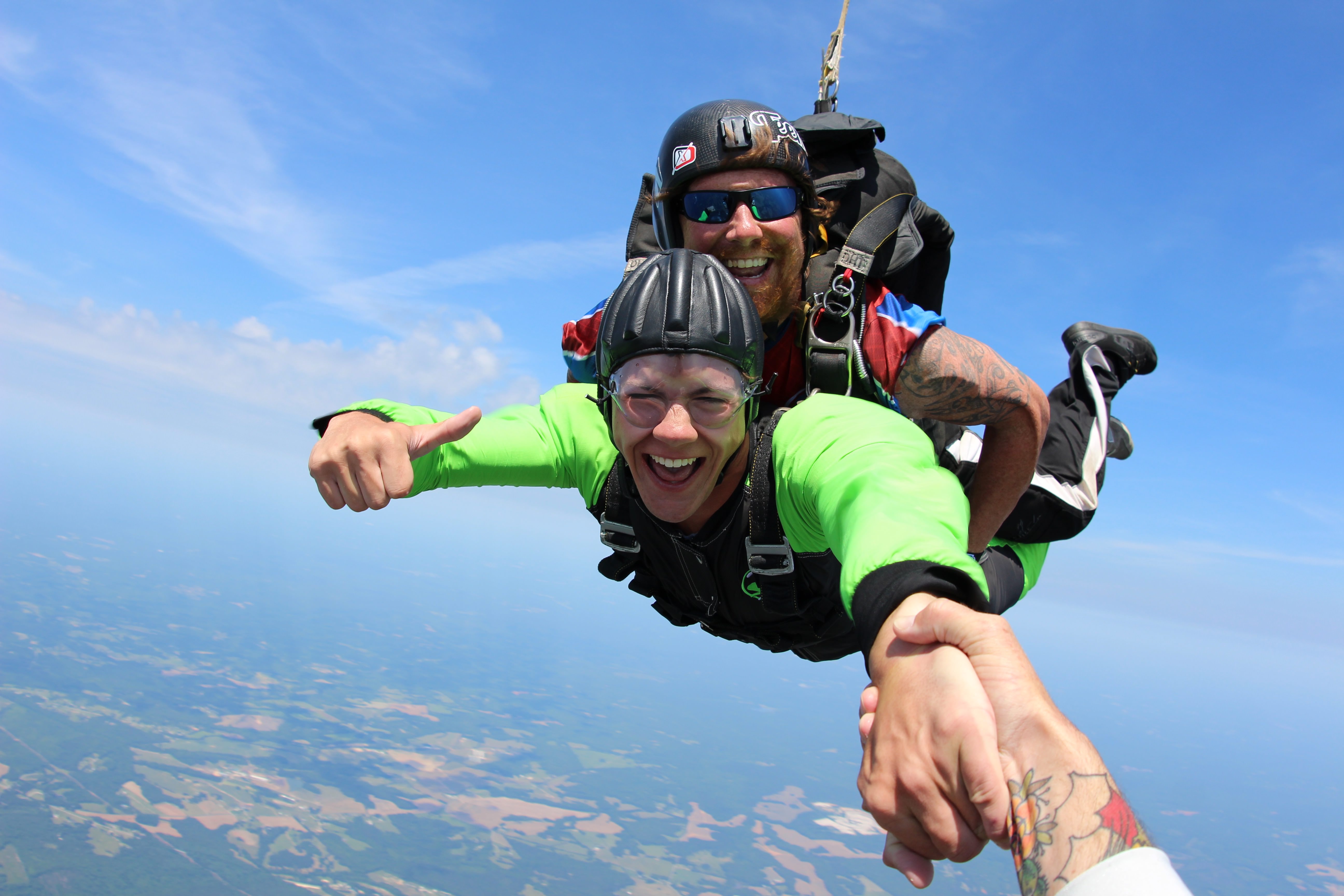 Tandem skydivers in freefall, student wearing a bright green jumpsuit 